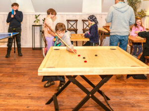 051 sala gier rodzinnych chlopiec gra w crokinole z tata ping pong dzieci w tle ostoja dwa jeziora kal wegorzewo mazury